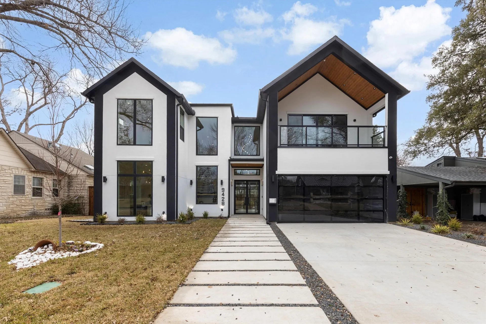 A modern Dallas house with white stucco, black trim and a concrete walkway leading to the front door.