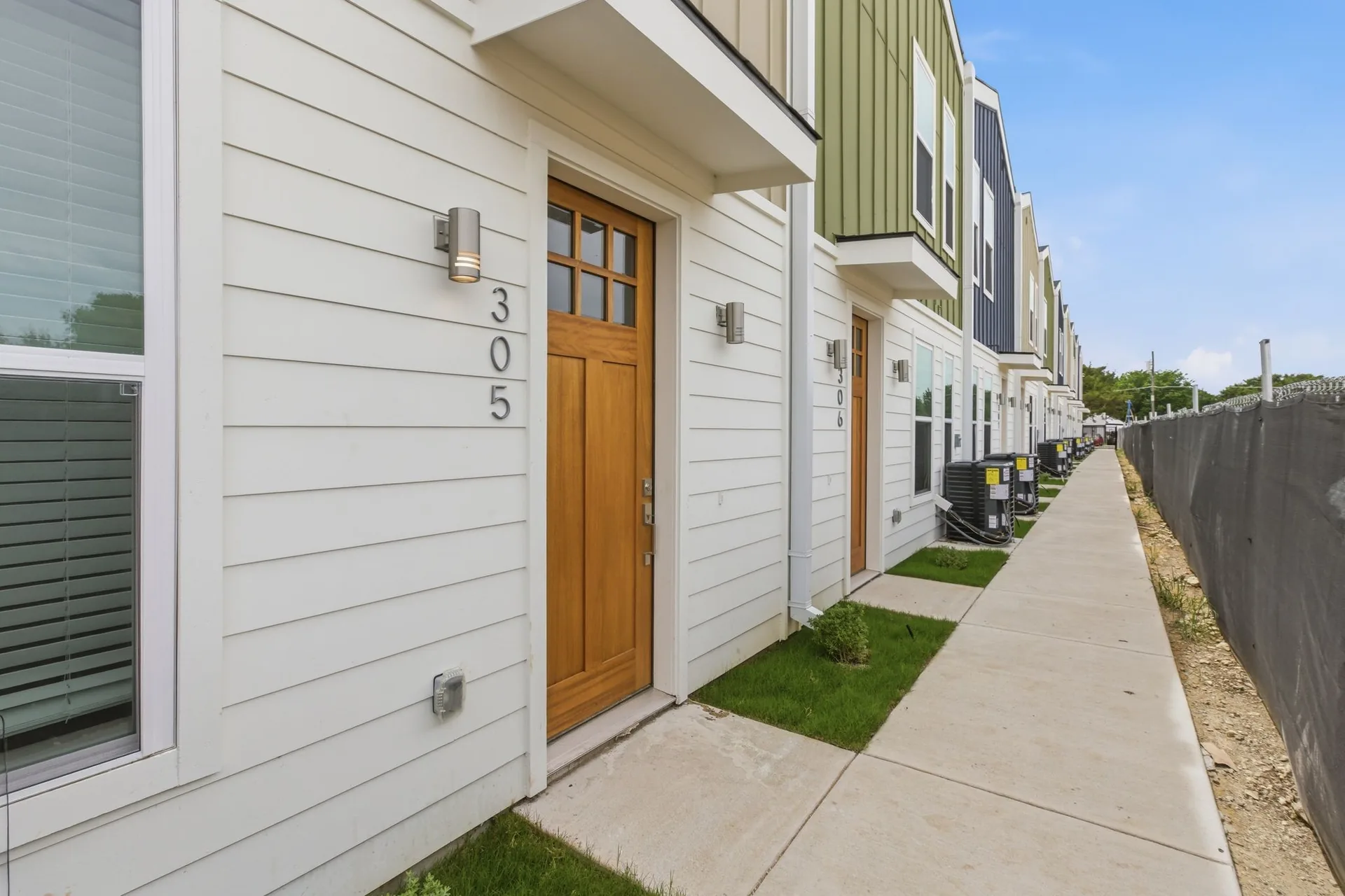 A row of newly built townhomes in white siding with dark trim along a paved walkway.