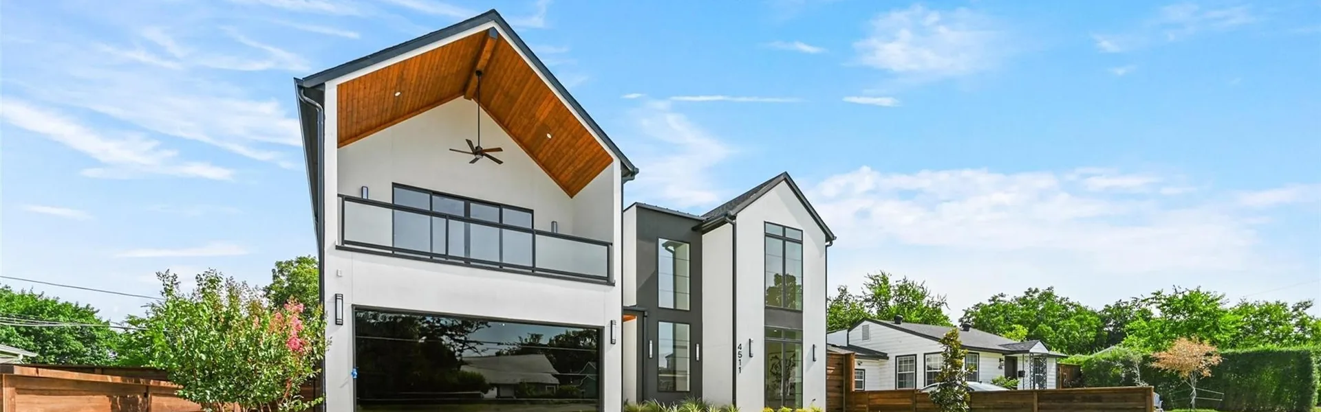 A modern Dallas house with a deep timber-lined gable over a glazed garage, beneath a blue sky.