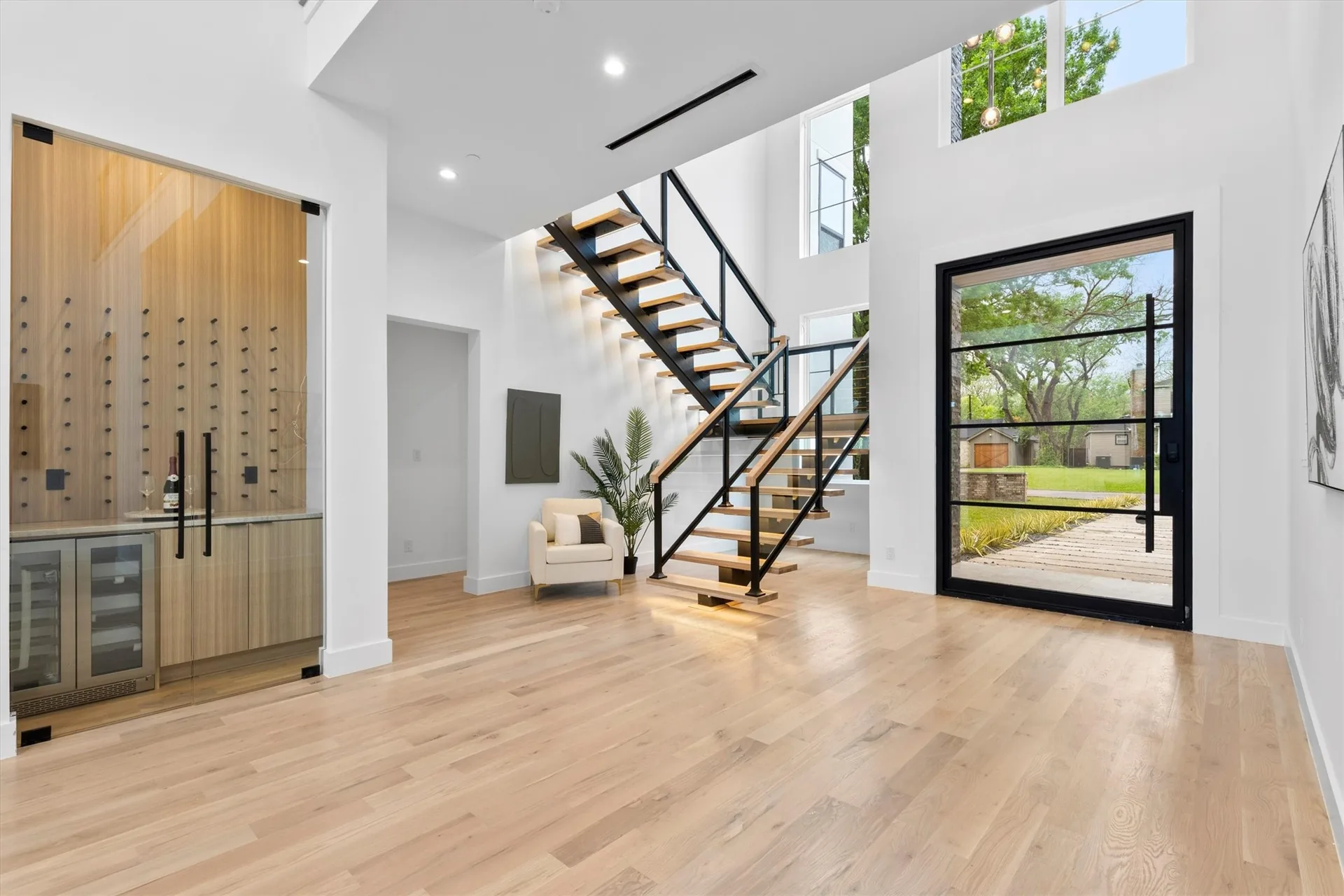 An entry hall with a floating staircase in black steel and oak, beside a glass-walled wine room.