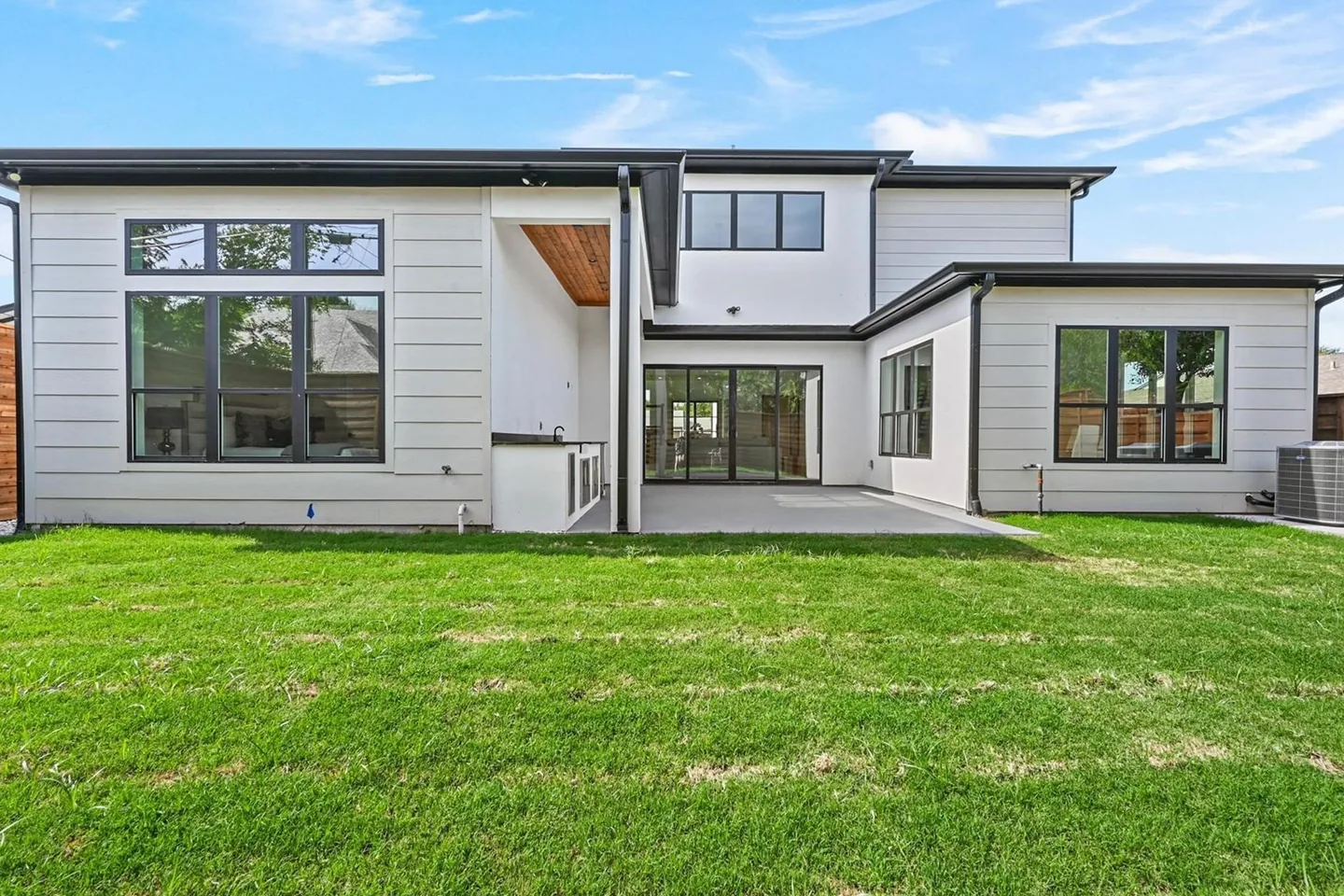 The rear of a modern Dallas house with a covered terrace looking across a lawn.