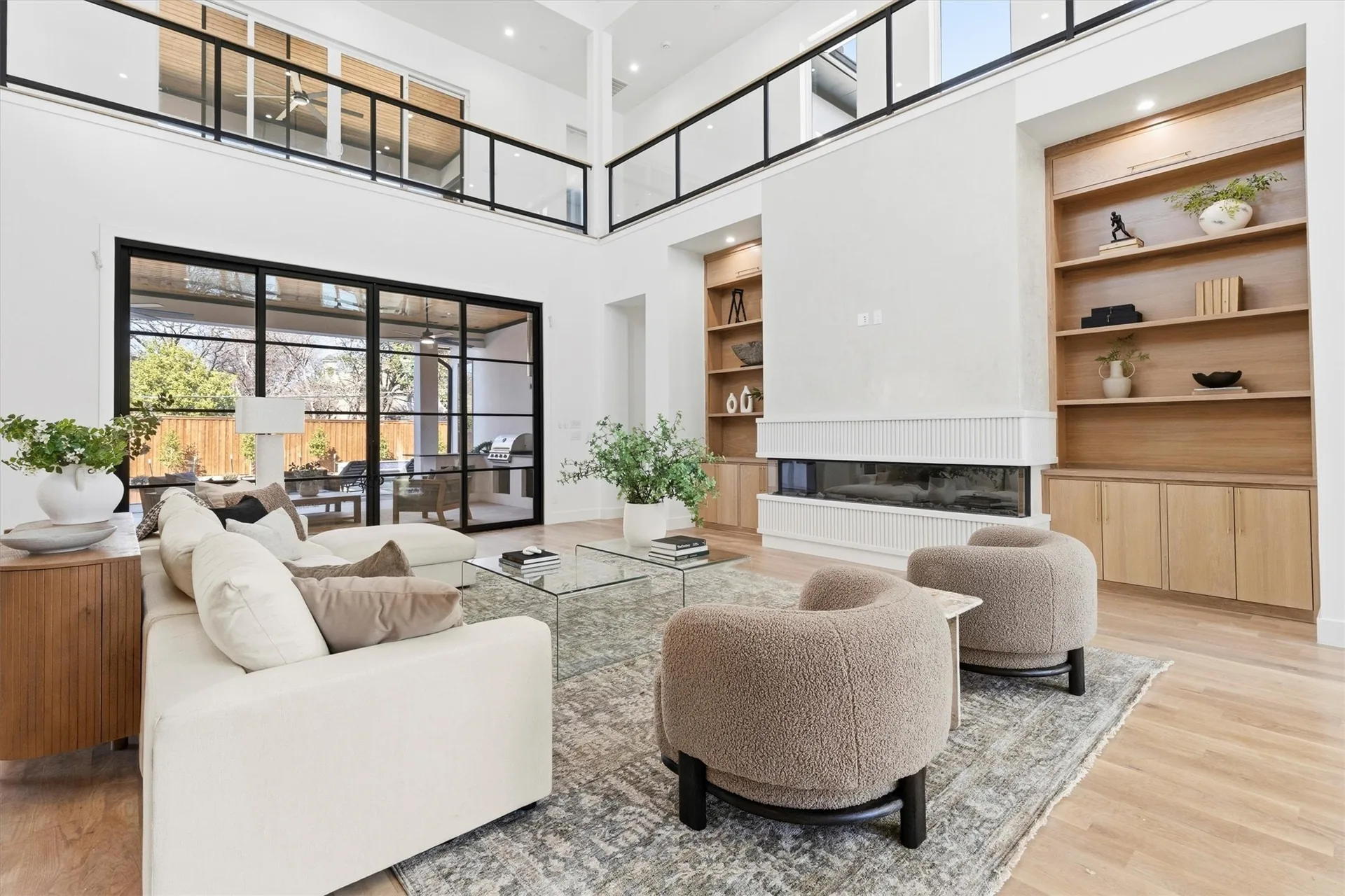 A double-height living room with white walls, oak shelving, a ribbed fireplace and a mezzanine gallery above.